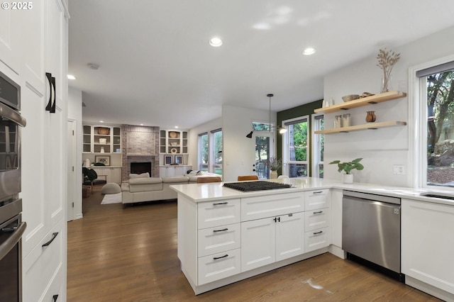 3840 NW Loy Ct, Portland, OR 97229 - kitchen featuring stainless steel appliances, a fireplace, a peninsula, dark wood-style flooring, and white cabinetry