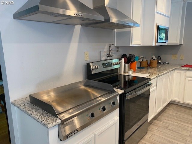 5944 SW Wilbard St, Portland, OR 97219 - kitchen with range with electric cooktop, wall chimney range hood, light wood-style floors, and white cabinets