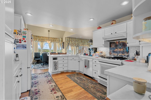 kitchen with white appliances, light wood-style flooring, a peninsula, white cabinets, and under cabinet range hood