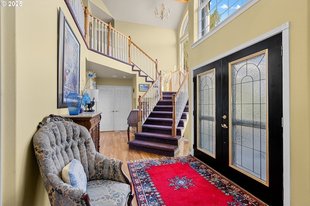 entryway featuring a towering ceiling, an inviting chandelier, stairway, french doors, and wood finished floors