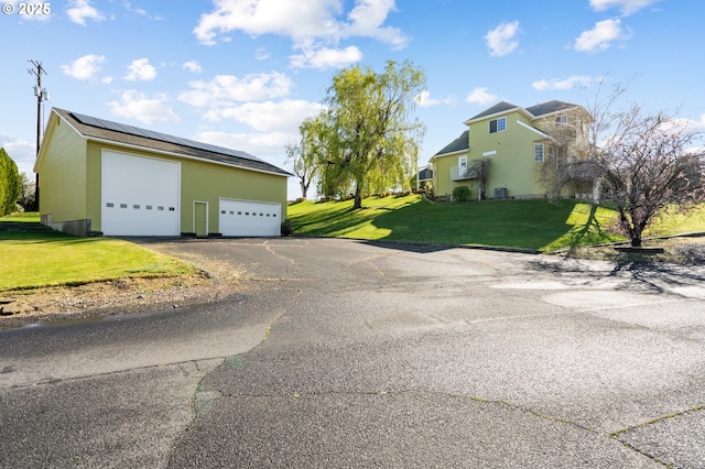 exterior space featuring a detached garage, solar panels, and a lawn