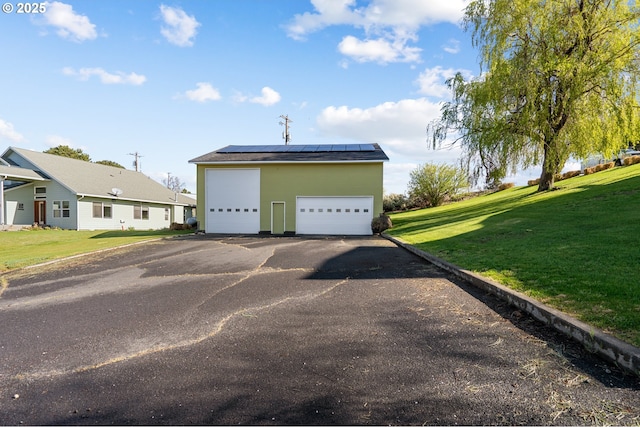 exterior space with roof mounted solar panels, an outbuilding, a front lawn, and a detached garage