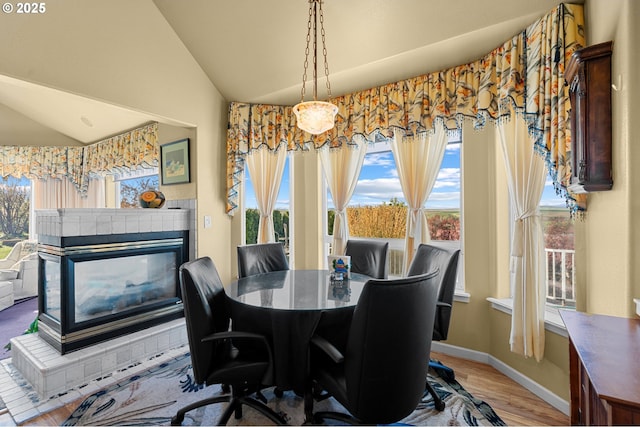 dining room featuring baseboards, wood finished floors, a tiled fireplace, and vaulted ceiling