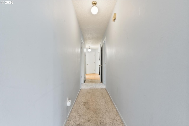 hall with a textured ceiling and light colored carpet