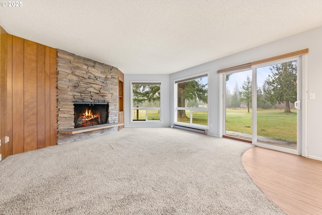 unfurnished living room with carpet, a baseboard heating unit, wooden walls, a stone fireplace, and a textured ceiling