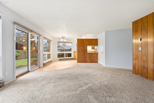 unfurnished living room with light carpet, a textured ceiling, wood walls, and a notable chandelier