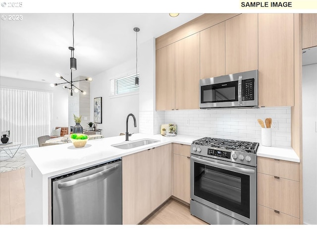 kitchen featuring appliances with stainless steel finishes, decorative light fixtures, sink, kitchen peninsula, and light brown cabinets