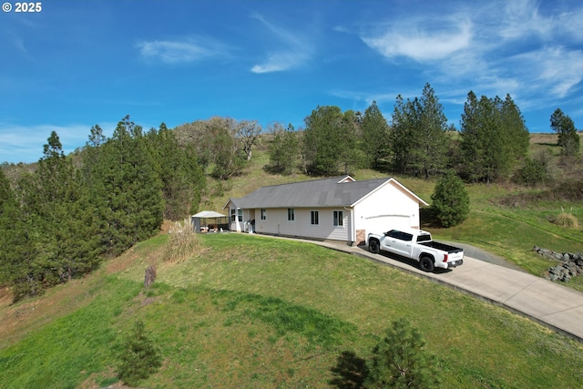 exterior space featuring concrete driveway, a front lawn, and a forest view