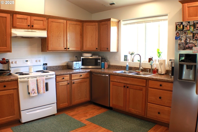 kitchen with a sink, brown cabinets, light wood finished floors, appliances with stainless steel finishes, and under cabinet range hood