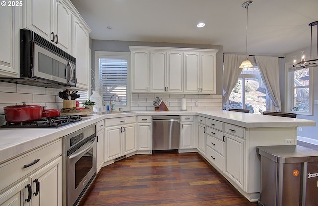 kitchen featuring dark wood-style flooring, a sink, a peninsula, stainless steel appliances, and tasteful backsplash