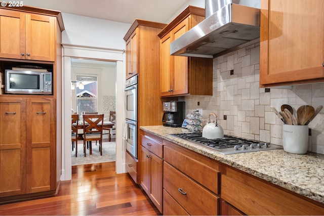 15475 SW Brighton Way, Beaverton, OR 97007 - kitchen featuring wall chimney range hood, stainless steel appliances, wood finished floors, decorative backsplash, and light stone countertops