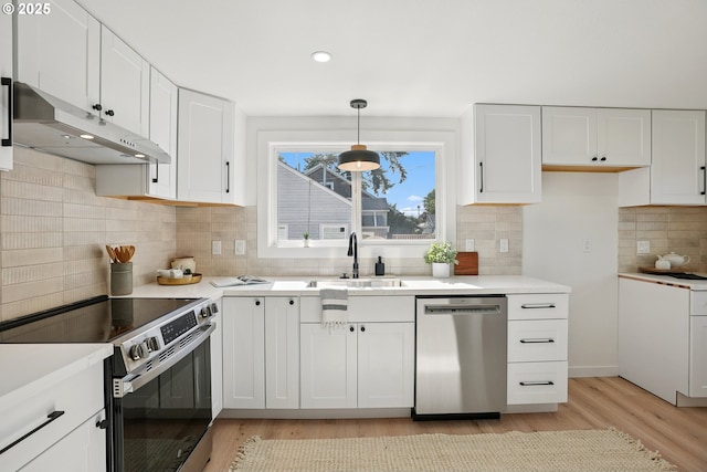 2615 N Gammans Pl, Portland, OR 97217 - kitchen with appliances with stainless steel finishes, under cabinet range hood, light wood finished floors, white cabinetry, and tasteful backsplash