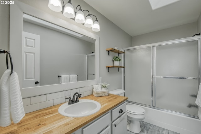 bathroom with toilet, backsplash, wood finished floors, shower / bath combination with glass door, and vanity