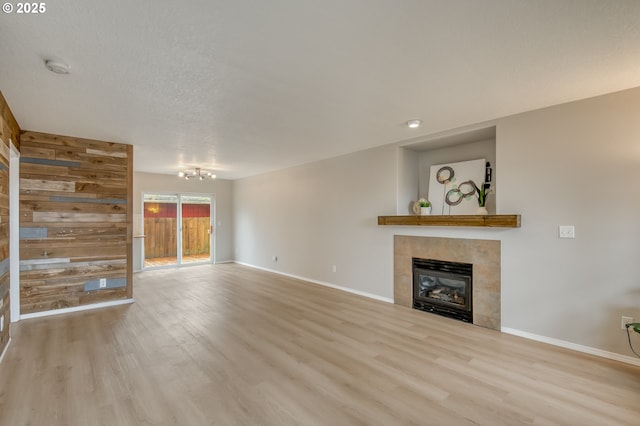 unfurnished living room featuring baseboards, wooden walls, wood finished floors, and a fireplace