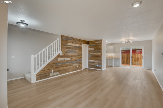 unfurnished living room featuring stairway, wooden walls, baseboards, and light wood finished floors