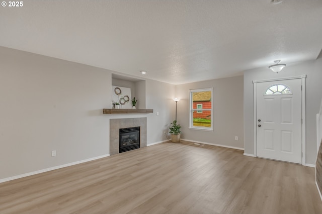 unfurnished living room featuring visible vents, baseboards, light wood-style flooring, and a tile fireplace