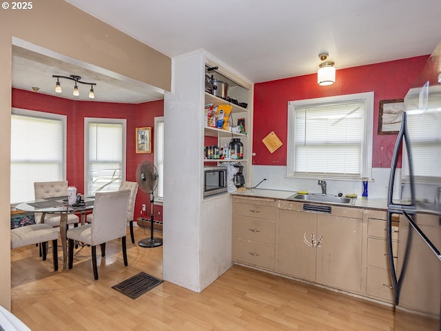 kitchen featuring light countertops, a sink, stainless steel microwave, freestanding refrigerator, and light wood-style flooring
