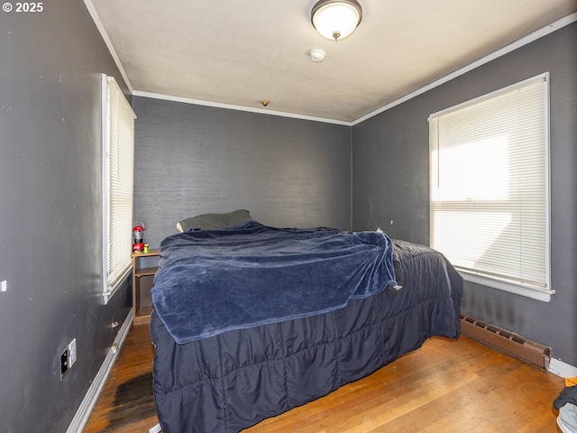 bedroom featuring a baseboard heating unit, baseboards, wood finished floors, and crown molding