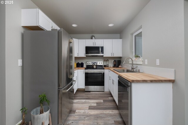 kitchen with butcher block countertops, sink, stainless steel appliances, white cabinets, and light wood-type flooring