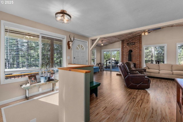 living area featuring wood finished floors, vaulted ceiling, a wood stove, and baseboards