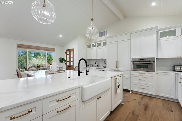 kitchen with oven, a sink, light wood finished floors, white cabinetry, and backsplash