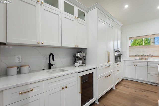kitchen with beverage cooler, a sink, stainless steel oven, white cabinets, and recessed lighting