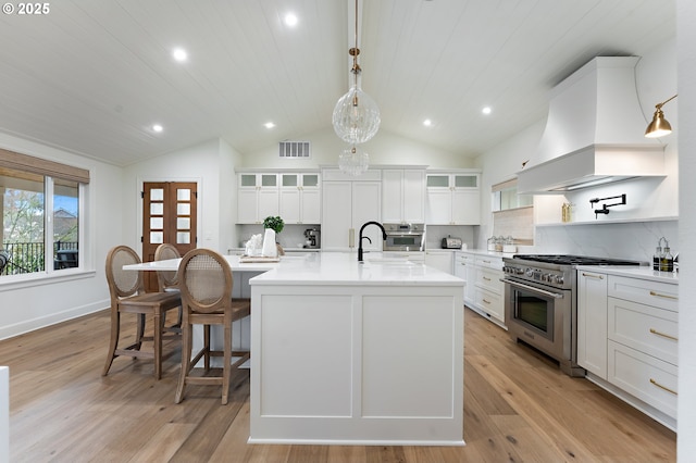 kitchen with stainless steel appliances, premium range hood, vaulted ceiling, a large island with sink, and light countertops