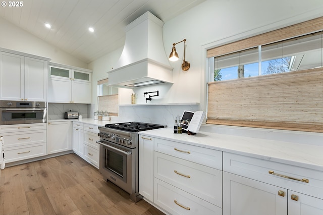 kitchen with stainless steel appliances, custom range hood, lofted ceiling, decorative backsplash, and white cabinetry