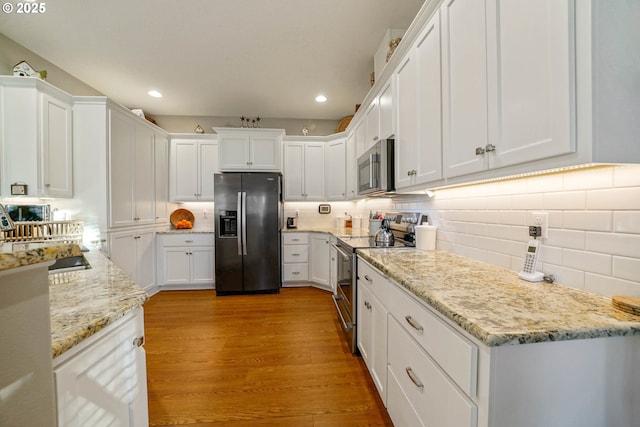 kitchen with stainless steel appliances, light stone countertops, light hardwood / wood-style flooring, and white cabinets