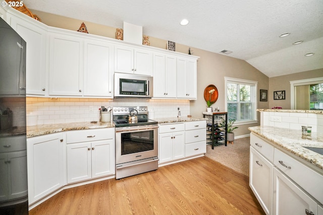 kitchen with appliances with stainless steel finishes, tasteful backsplash, white cabinets, vaulted ceiling, and light wood-type flooring