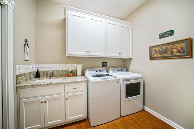 laundry area featuring cabinets, sink, washing machine and clothes dryer, and light hardwood / wood-style floors