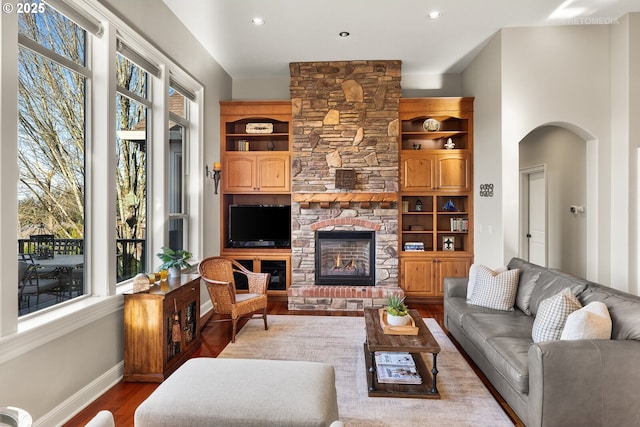 living area featuring wood finished floors, a fireplace, baseboards, recessed lighting, and arched walkways