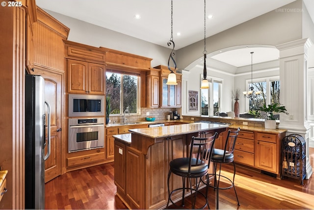 kitchen with a kitchen island, arched walkways, a sink, dark wood finished floors, and appliances with stainless steel finishes