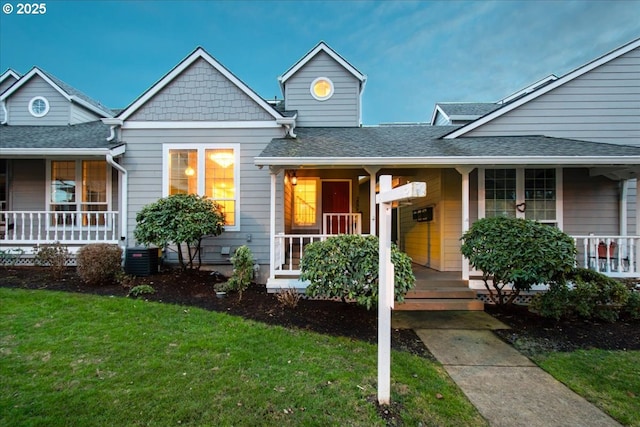 view of front of home with central AC, a porch, a front yard, and a shingled roof