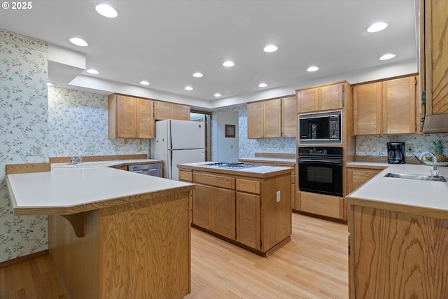 kitchen featuring light wood-style floors, a sink, black appliances, and wallpapered walls