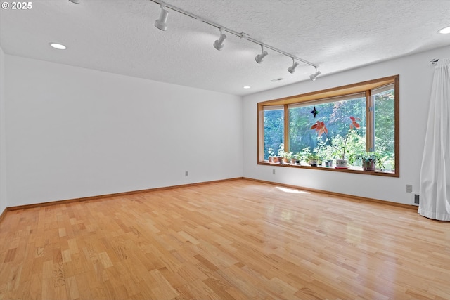 empty room with light wood-type flooring, a textured ceiling, baseboards, and recessed lighting