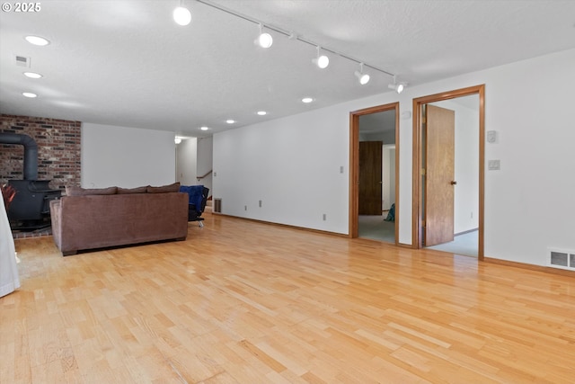 living room with light wood-type flooring, a wood stove, visible vents, and a textured ceiling