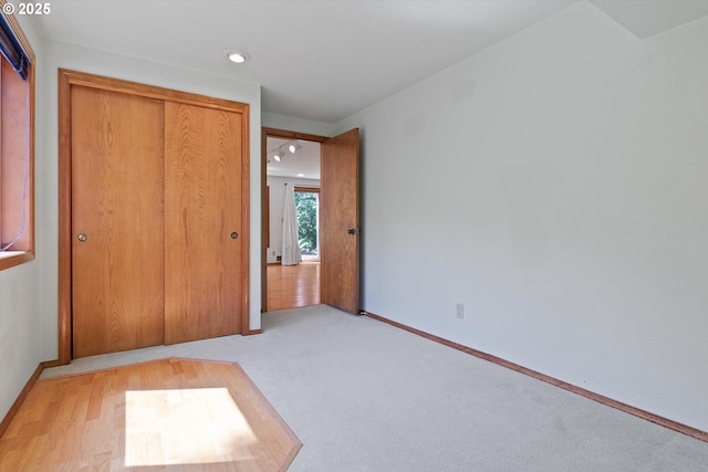 unfurnished bedroom with light wood-style floors, a closet, light carpet, and baseboards