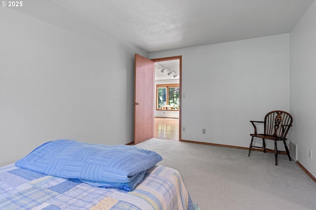 carpeted bedroom with rail lighting, visible vents, baseboards, and a textured ceiling