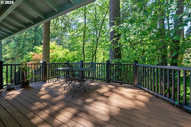 wooden terrace featuring outdoor dining space and a wooded view