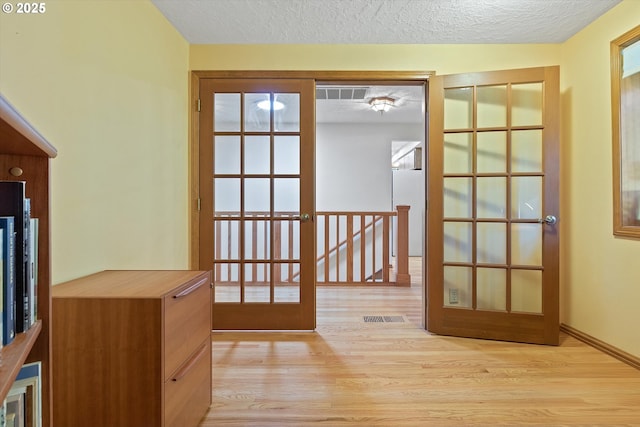 doorway with baseboards, light wood-style flooring, visible vents, and a textured ceiling