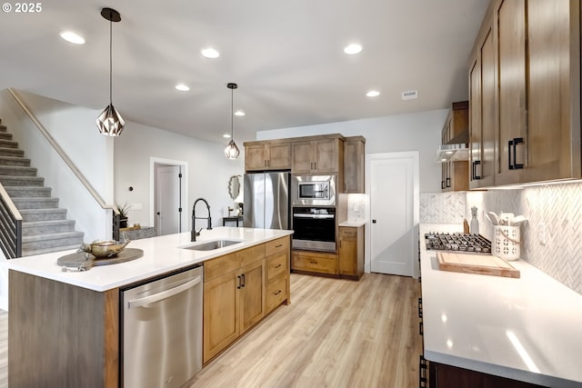 kitchen with sink, tasteful backsplash, an island with sink, pendant lighting, and stainless steel appliances