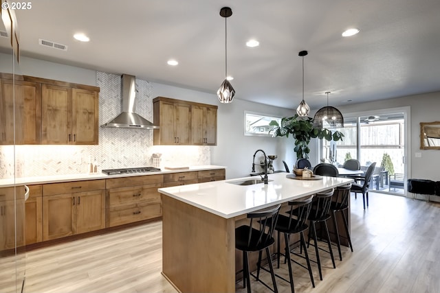 kitchen with a breakfast bar, tasteful backsplash, an island with sink, sink, and wall chimney range hood