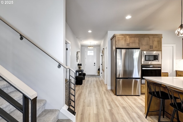 kitchen featuring decorative light fixtures, light wood-type flooring, a breakfast bar area, and appliances with stainless steel finishes