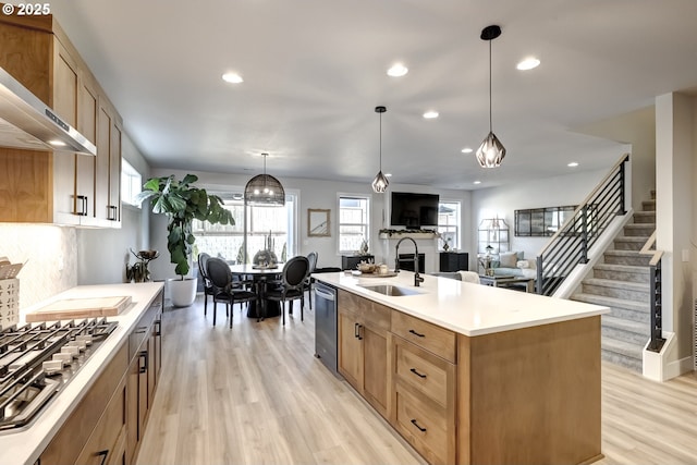 kitchen with hanging light fixtures, an island with sink, wall chimney exhaust hood, and appliances with stainless steel finishes