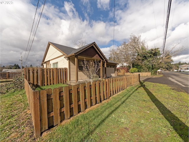 view of side of home featuring a fenced front yard, a yard, and an attached garage