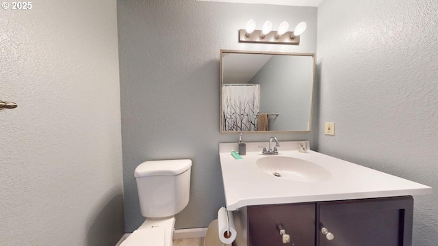 full bathroom featuring vanity, toilet, and a textured wall