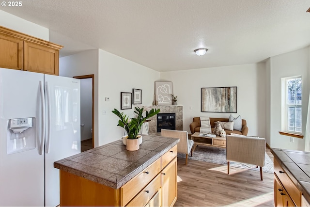 kitchen featuring tile counters, white refrigerator with ice dispenser, a tile fireplace, and light wood-type flooring