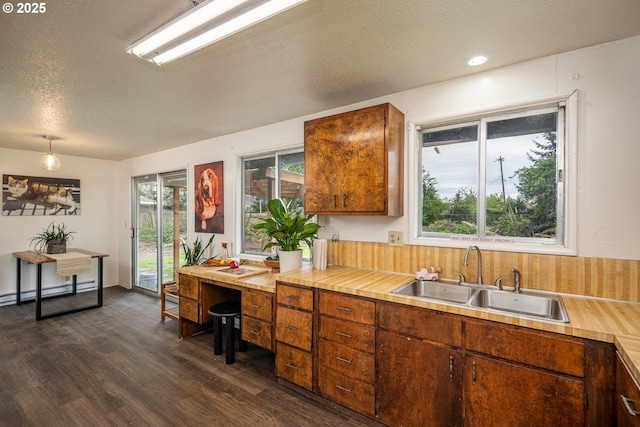 kitchen featuring light countertops, a sink, brown cabinetry, a textured ceiling, and dark wood-style flooring