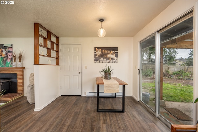 interior space with a baseboard heating unit, a brick fireplace, dark wood-style floors, and a textured ceiling